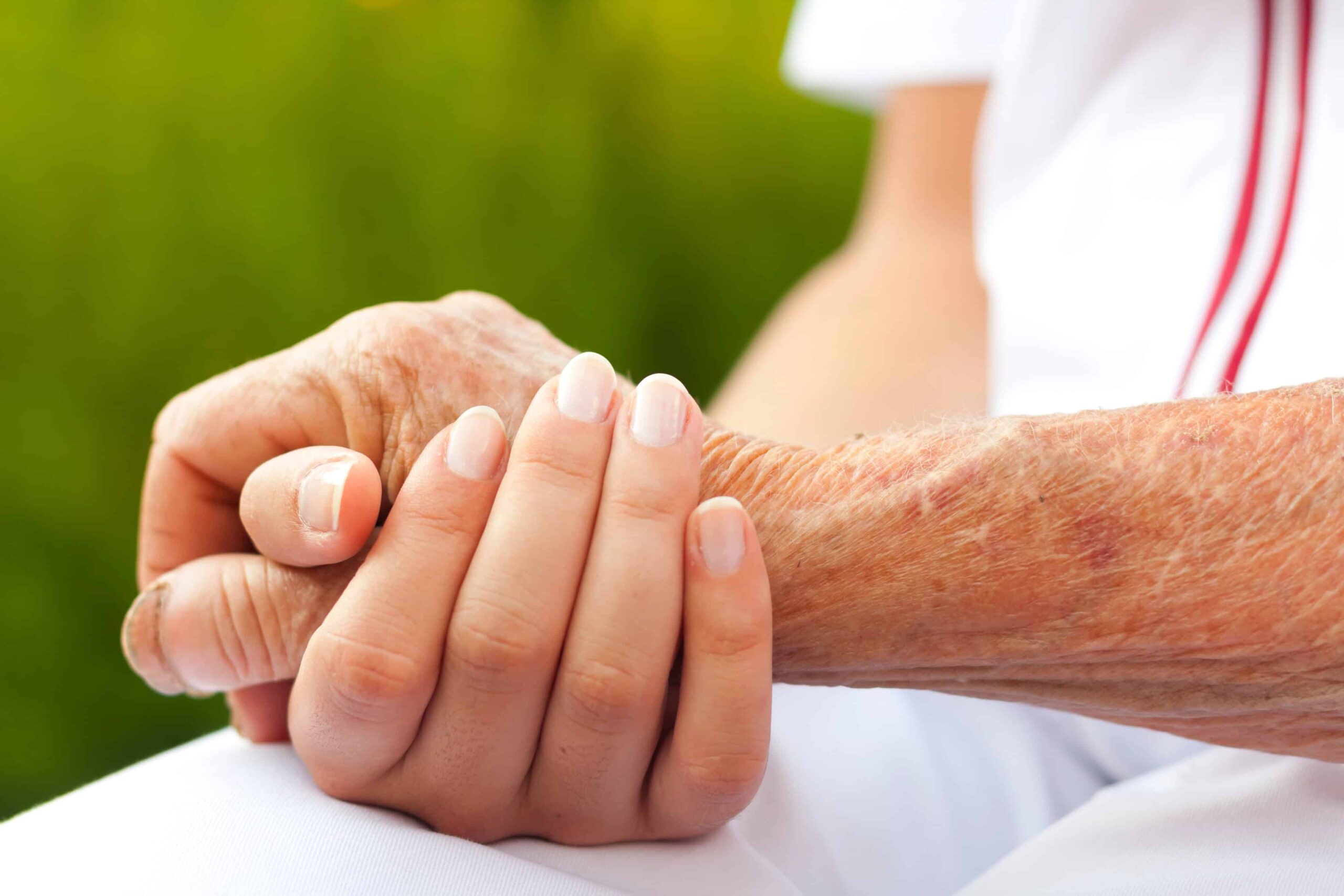 A caregiver holds the hand of an elderly patient as they offer social and spiritual services in support of the patient